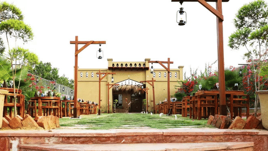 Outdoor walkway at Themis Mudhouse Resorts featuring rustic wooden lamp posts, potted plants, and a village-style mud entry archway.