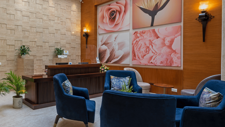 Hotel Saket 27 lounge with armchairs, wooden desk, potted plants, and large floral artwork on the wall.