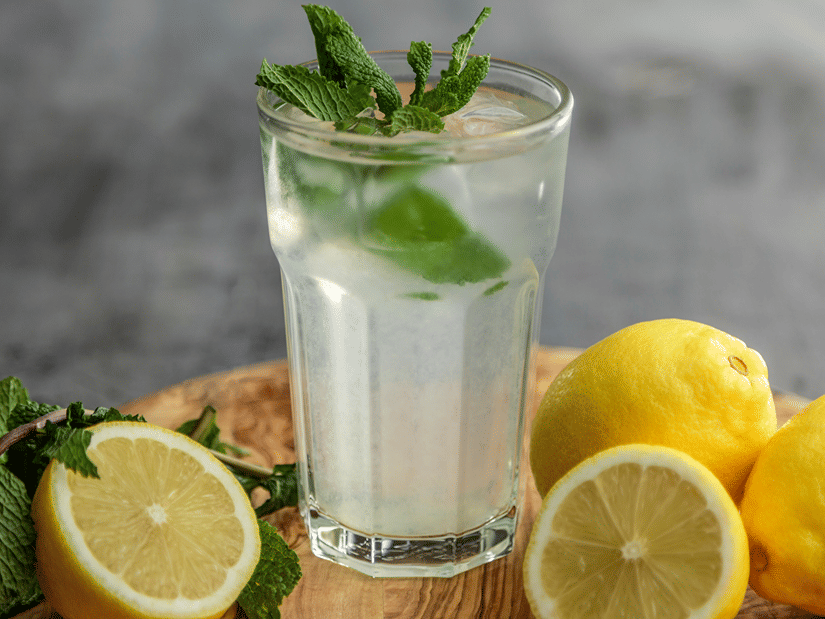 A glass of lemon water with fresh mint beside halved and whole lemons