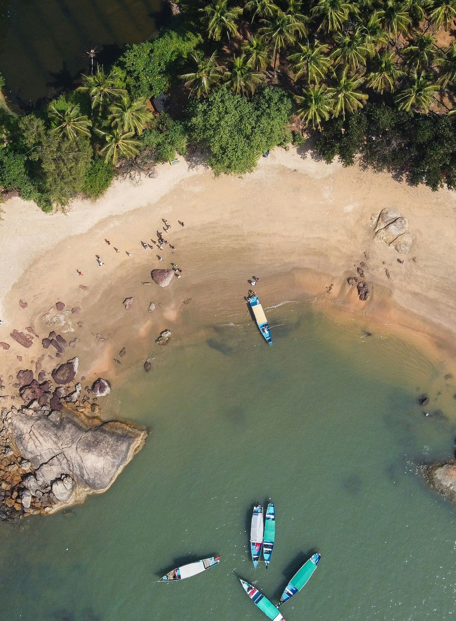 An aerial view of paradise beach with boats on the water and forest cover next to the beach