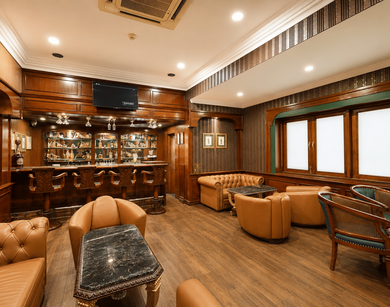 Cavalry Bar with backlit bottle shelves, carved wooden stools, tan leather seating, marble-topped tables and wood panelling at MAYFAIR Garden, Rourkela.