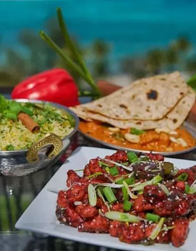 Variety of Indian dishes with vegetables, bread, and chutney, placed outdoors with a sea view | A Stone's Throw Away