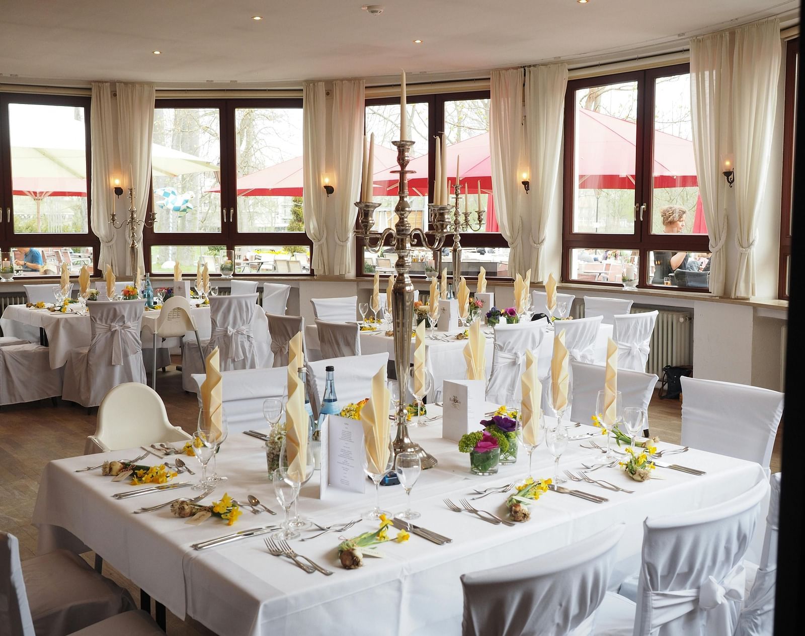 A bright banquet hall is set for a formal event with tall candle centrepieces and white tablecloths.