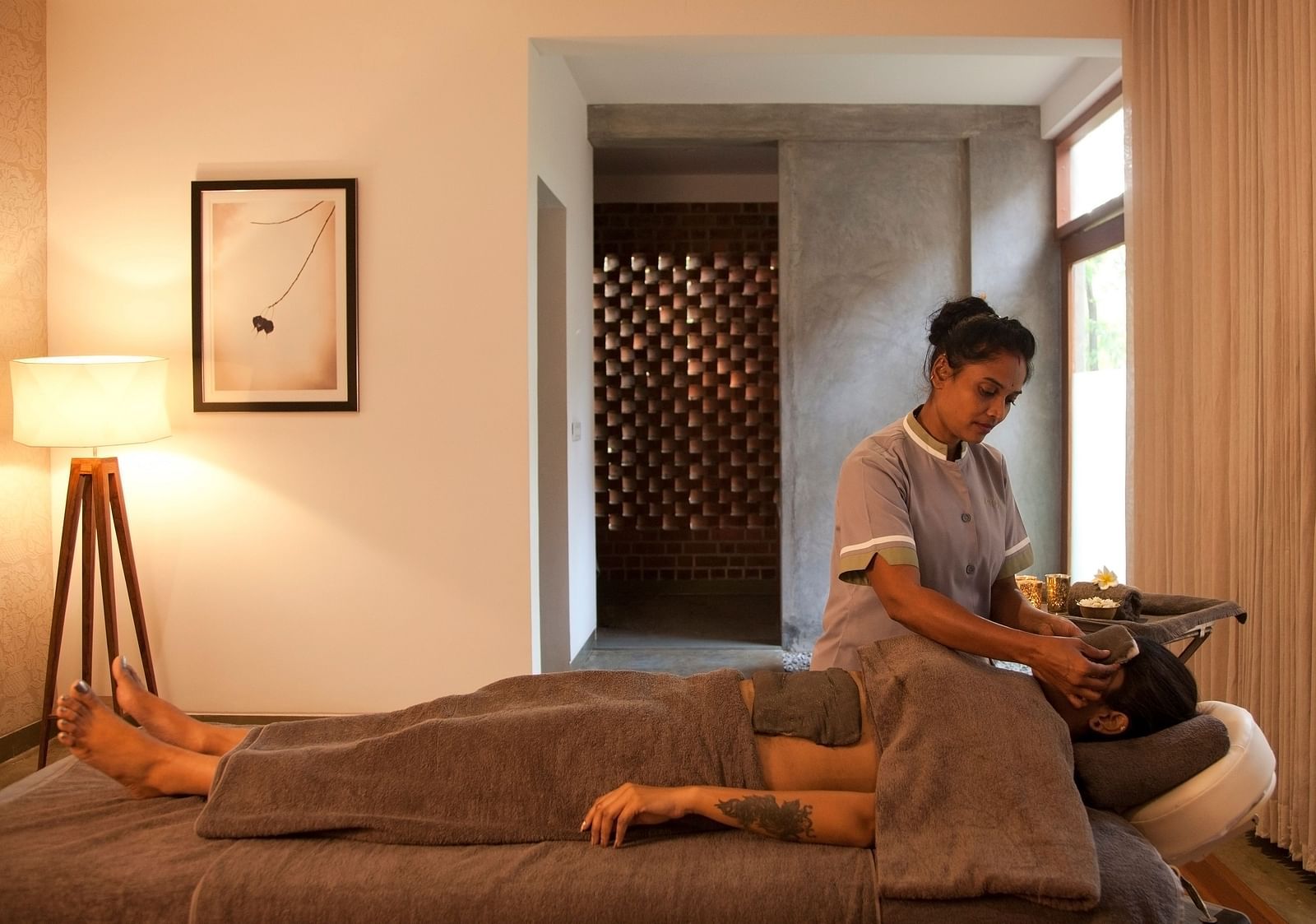 Person receiving head massage on massage table in room with lamp, picture frame, and window - Shreyas Retreat