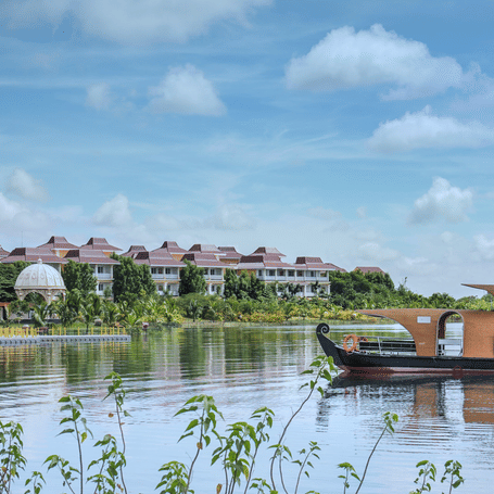 Panoramic view of MAYFAIR Lake Resort Raipur showing the lakeside villas and a traditional boat on the water.