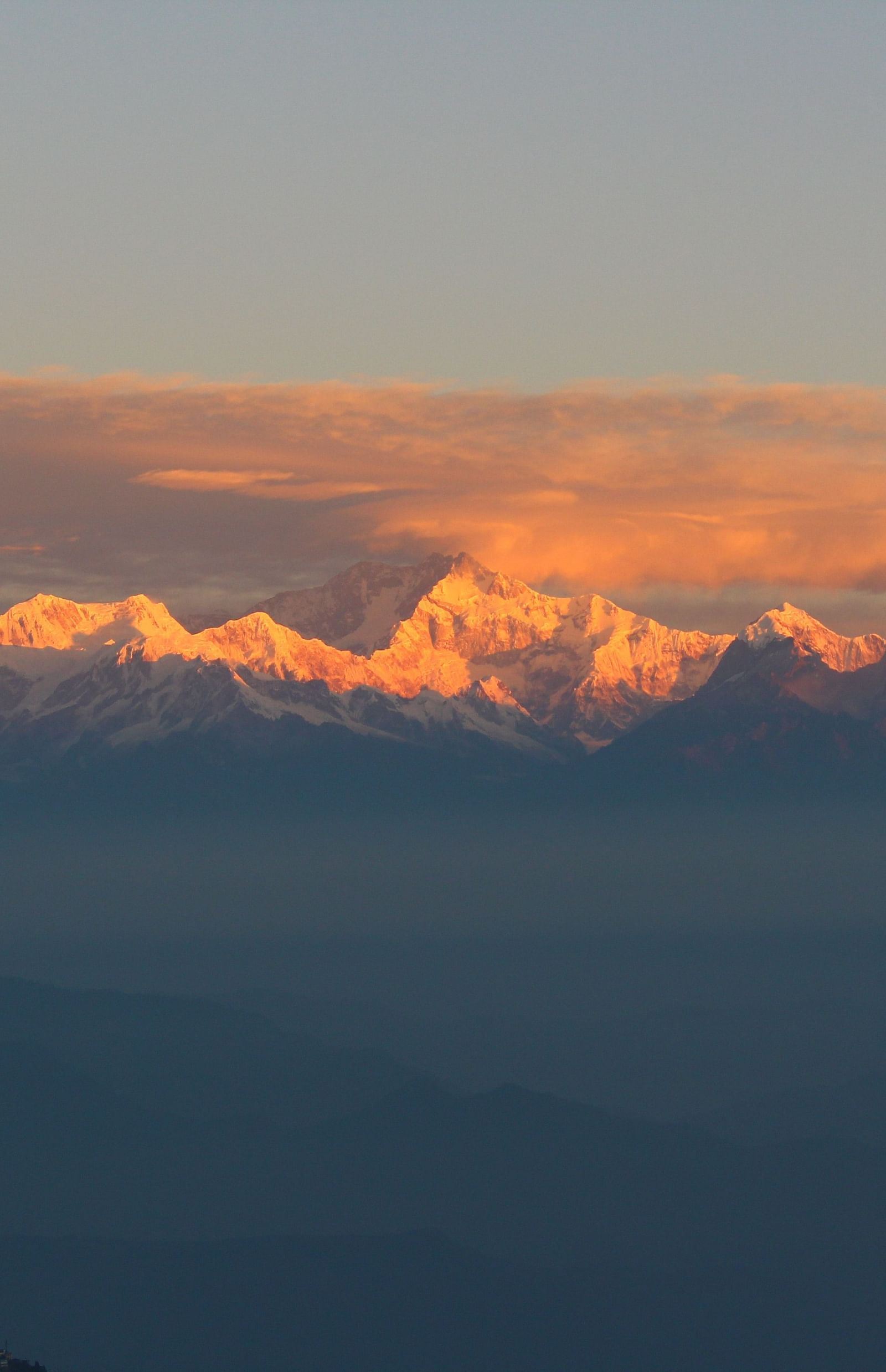 A far shot of mountains with a backdrop of peachy hues of the sky