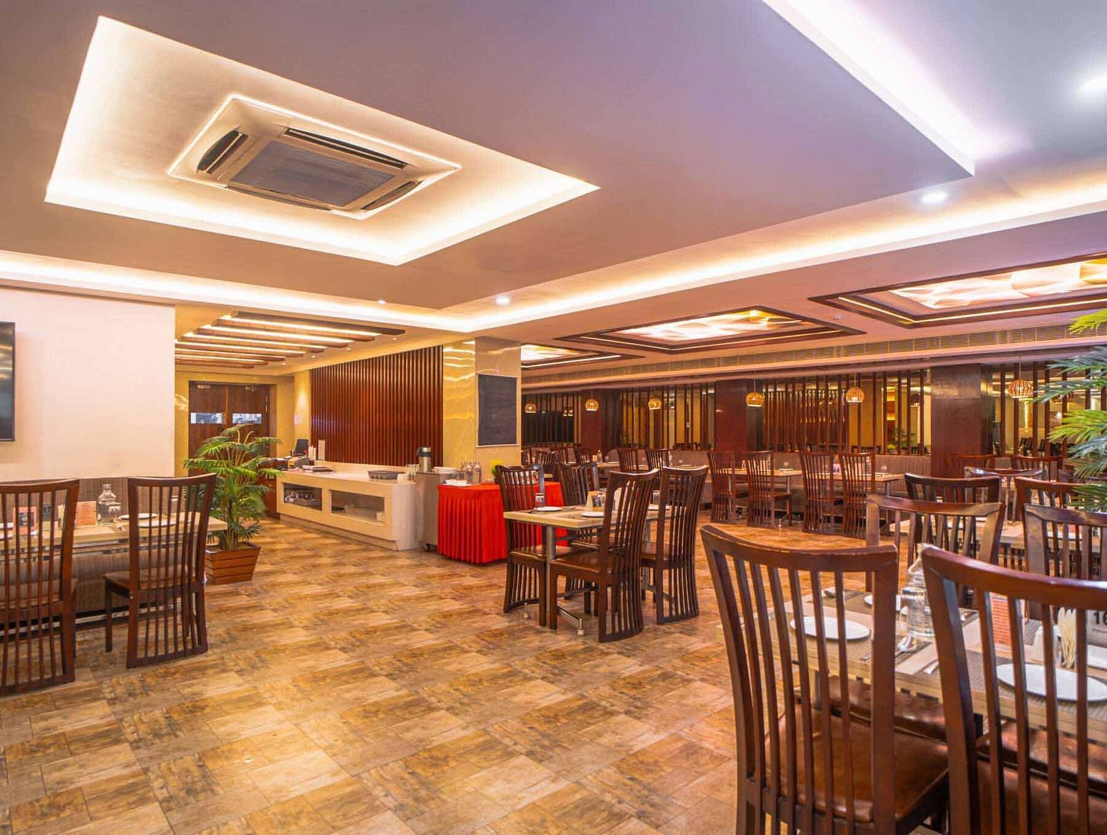A wide shot of a spacious dining area with wooden tables and chairs, illuminated by warm ceiling lights at Mansha Hotel Regency.