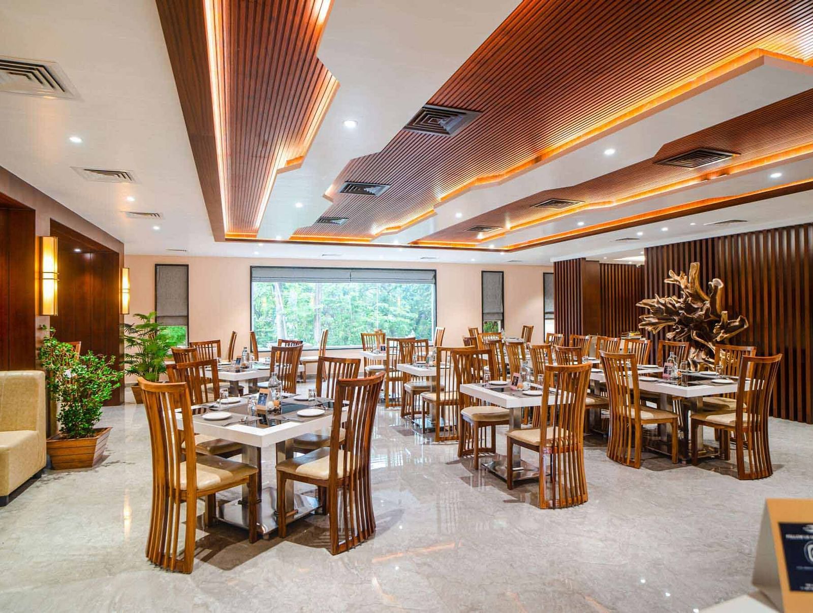 The warmly lit dining area of Pakeezah Restaurant at Mansha Palace features neatly set tables and comfortable wooden chairs.