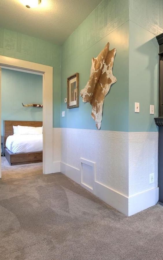 he Groveland Hotel's living area showcases sage green walls, an ornate black fireplace, mounted TV, and distinctive animal hide wall decor.