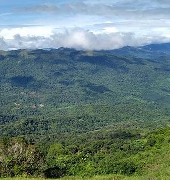 A lush, green mountainous landscape under a cloudy sky, showcasing the natural beauty of a hilly region.