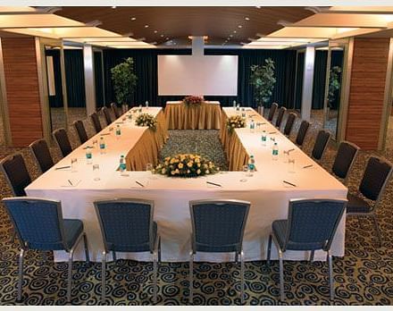 Shot of an expansive conference room at Mirage Hotel featuring a large table with chairs around it along with a projector on the wall. | Mirage Hotel