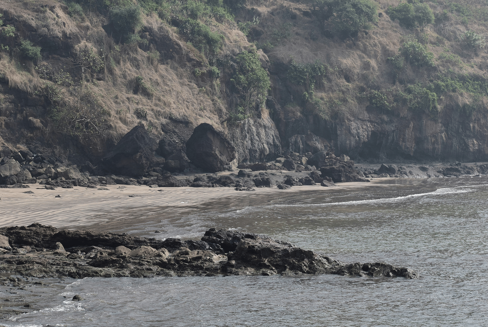 an overview of Alibaug Beach with rocks near the waters and mountains in the background