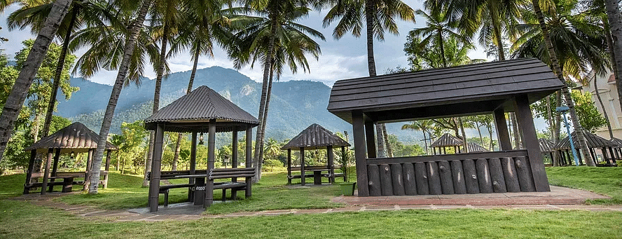 Scenic view of wooden gazebos under palm trees with mountains in the background and lush green grass in the foreground at Avana Resort