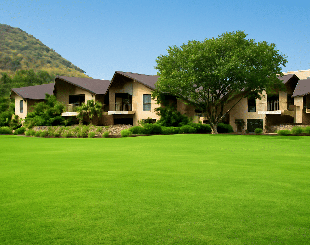 A well-manicured lawn stretches in front of a building complex, set against a backdrop of hills | Wedding Garden | The Qualia Resort Club & Brewery, Udaipur