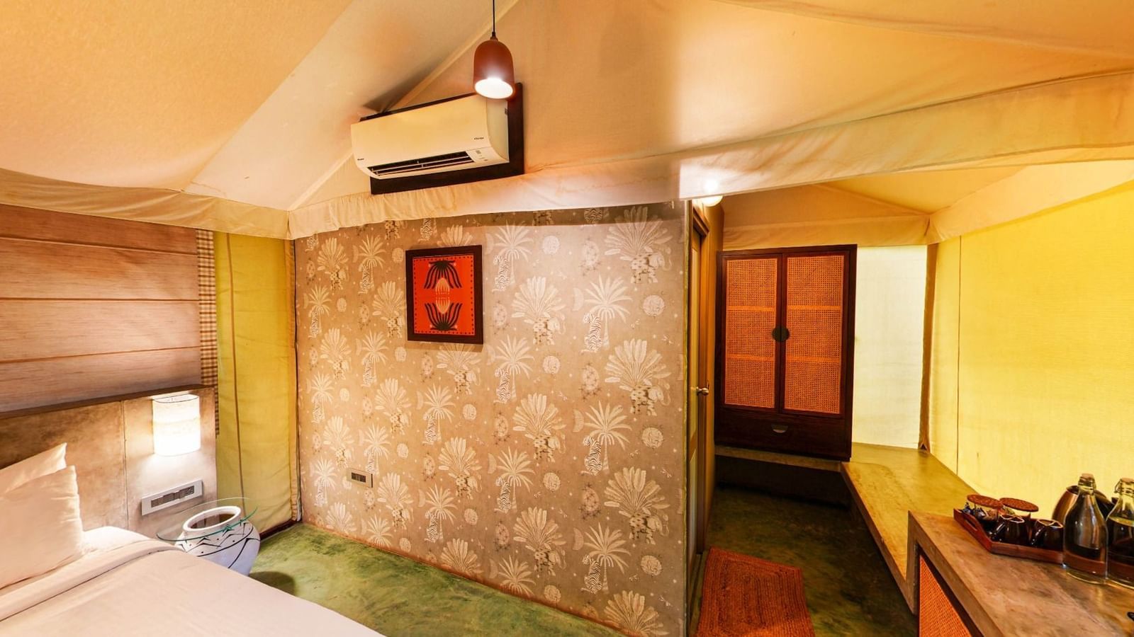 Interior of a tent room with yellow canvas walls, bed, A/c and luggage rack at Fireflies Resorts, Kabini.