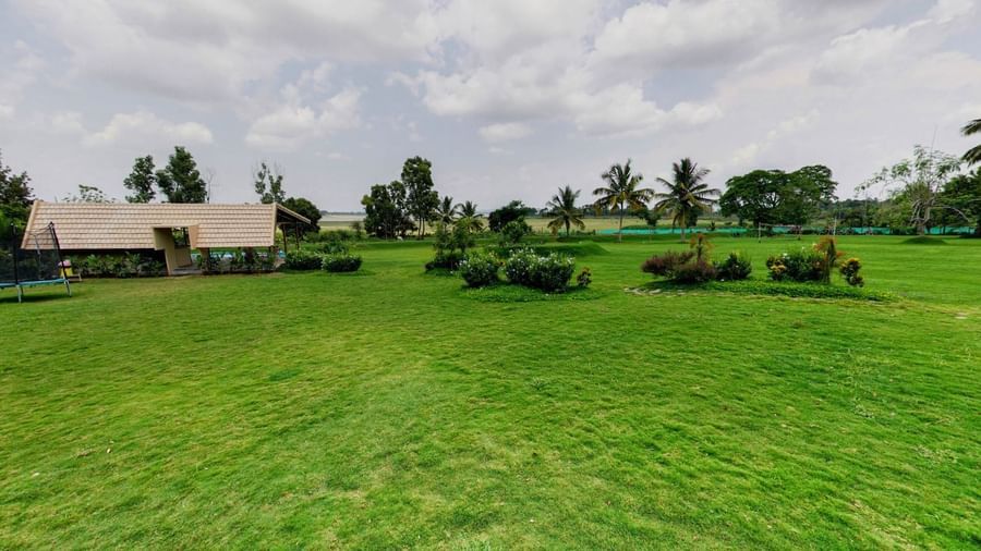 Expansive lawn with trimmed grass, scattered plants, and a single-storey building in the distance at Fireflies Resorts, Kabini.