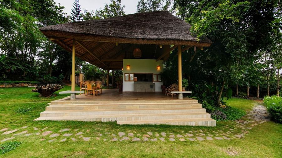 Open wooden reception area with steps and tiled flooring surrounded by greenery at Fireflies Resorts, Kabini.