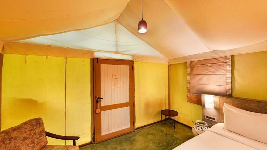 Tent room with sloped ceiling, king size bed, and wooden furniture beside the door at Fireflies Resorts, Kabini.