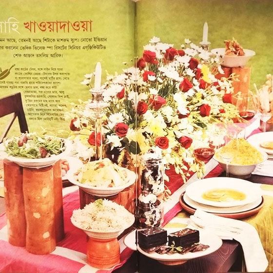 A bengali newspaper featuring a banquet table filled with food at Vedic Village Spa Resort.