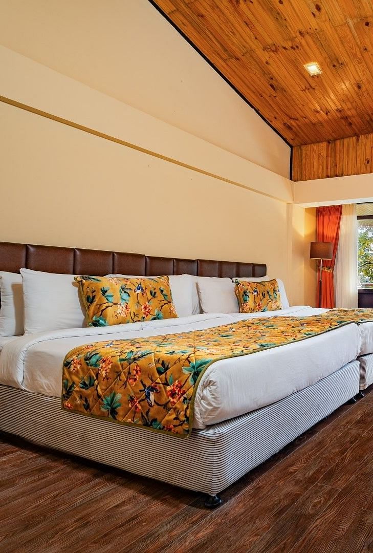 Family room with balcony offering stunning views, double bed, wooden bedside table, warm lighting, reading table with attached chair, and television with table at Summit Norling Resort & Spa, Gangtok.