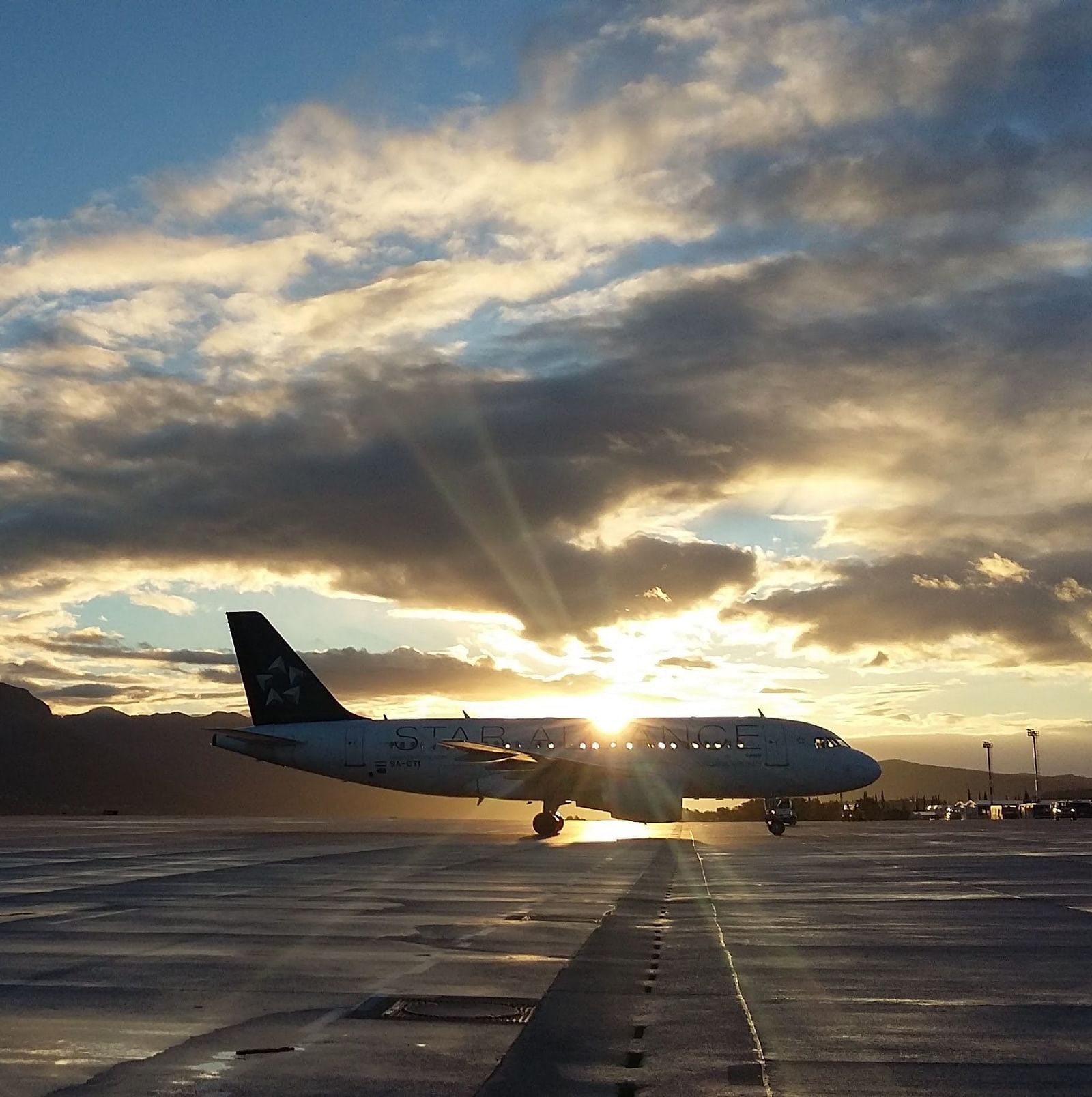 an aeroplane parked in a runway with the sun setting in the background
