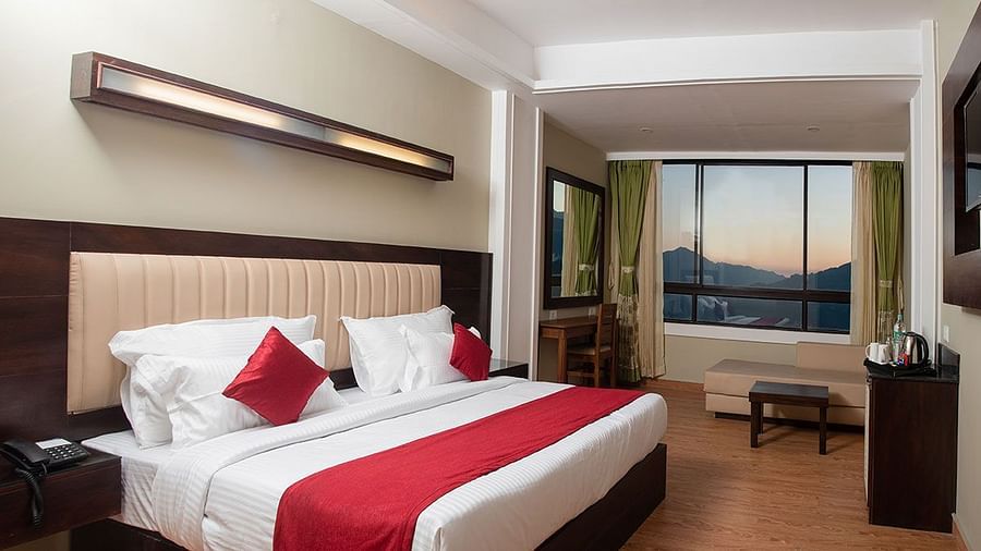 A room in Gangtok featuring a plush bed, bright lighting, a wall-mounted television, and a window with stunning views - Summit North Star, Gangtok