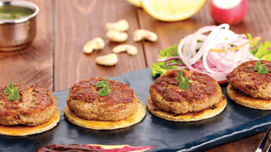 Kumbh Haleem ke Kebab served on a plate, garnished with fresh coriander and sliced onions.
