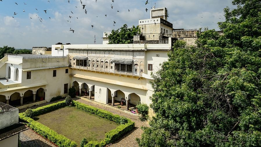 A bird's-eye view of Fort Barli reveals its courtyard, white buildings, and surrounding landscape under a partly cloudy sky.