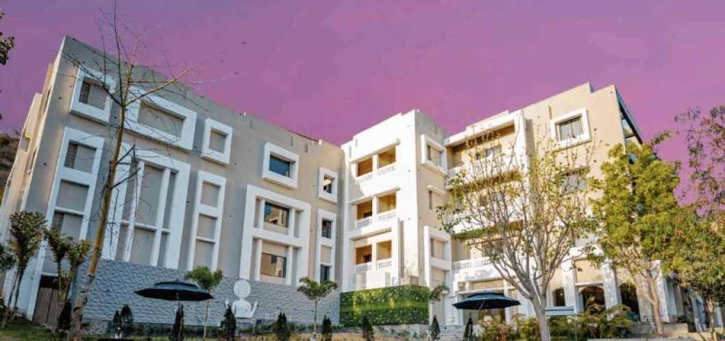Facade of Essentia Luxury Resort and Spa, Udaipur with trees on the side.
