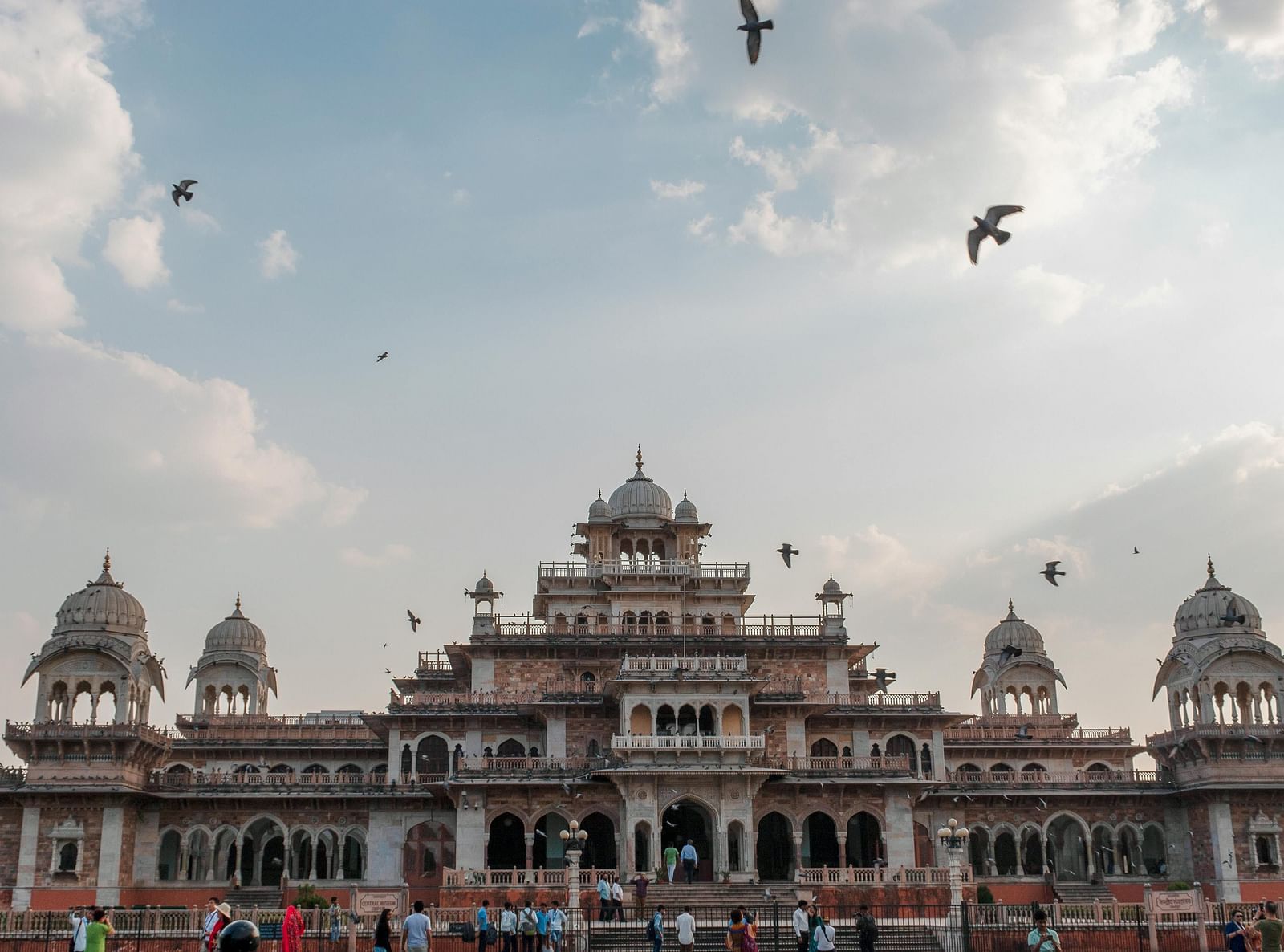 Exterior of a palace during a cloudy day with birds flying over it