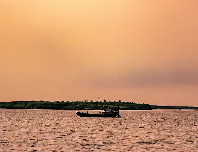 A small boat floating on tranquil waters with a beautiful orange-hued sunset in the background.