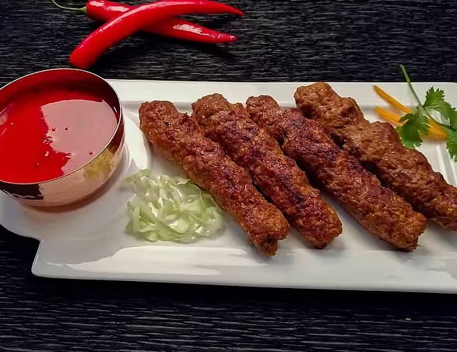 Close-up of Kebab served with a bright red chutney, and red chili peppers on a dark background.