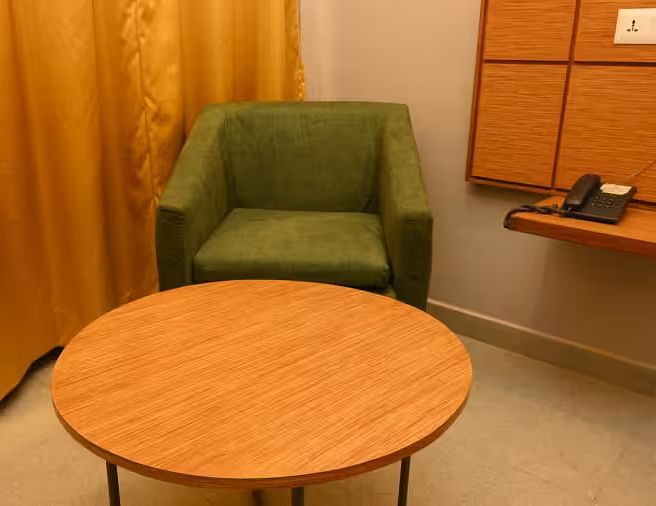  A cosy seating space with a round wooden table and a comfortable green armchair - Max Hotel Prayagraj.