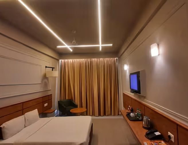 View of a modern hotel room with ambient lighting, a comfortable bed, and a wall-mounted TV - Max Hotel Prayagraj.
