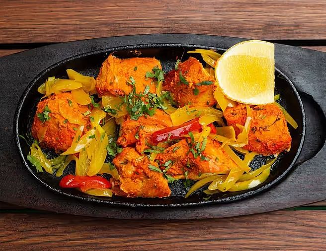 An Indian chicken dish served on a sizzling plate with lemon and vegetable garnishes.