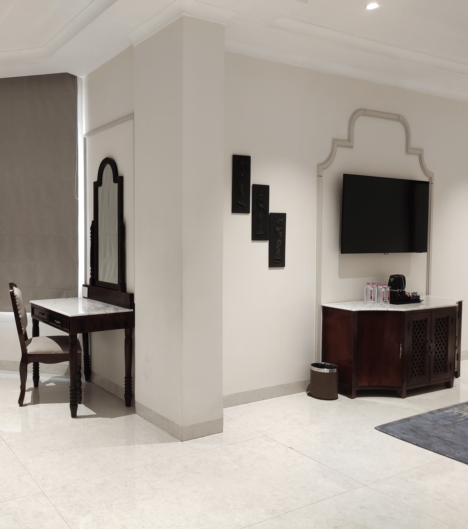 A view of a room at Anant Mahal, Jaipur with a wall mounted television, black decorative wall accents,a mirror, a wooden dressing table and chair.