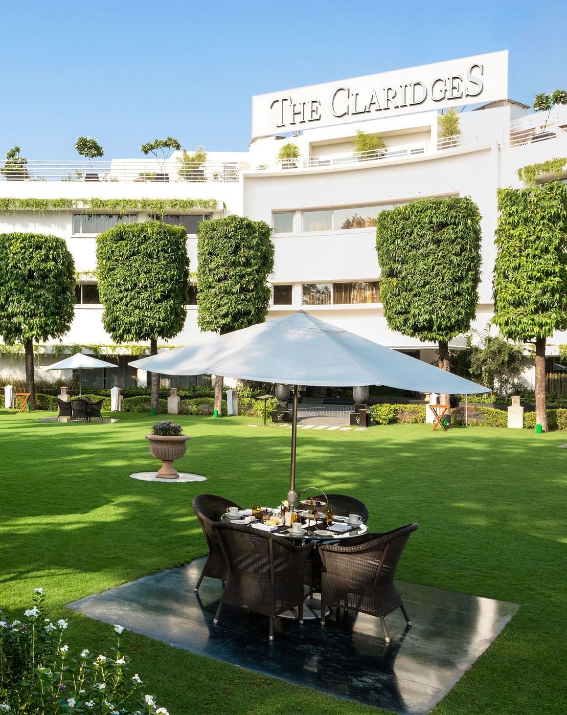 a beautiful landscape image of the claridges garden with glass top coffee tables scattered everywhere - The Claridges New Delhi