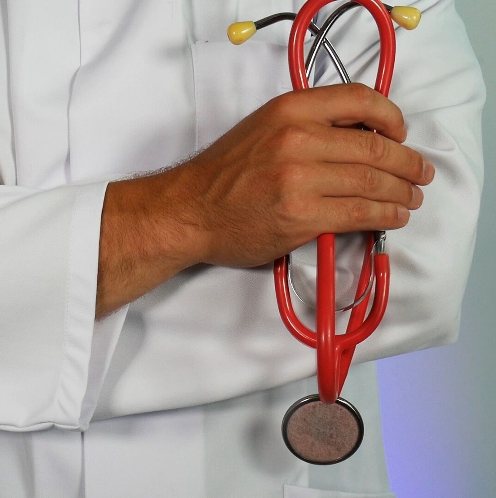 a close up image of a doctor with folded hands hoding a stethoscope 