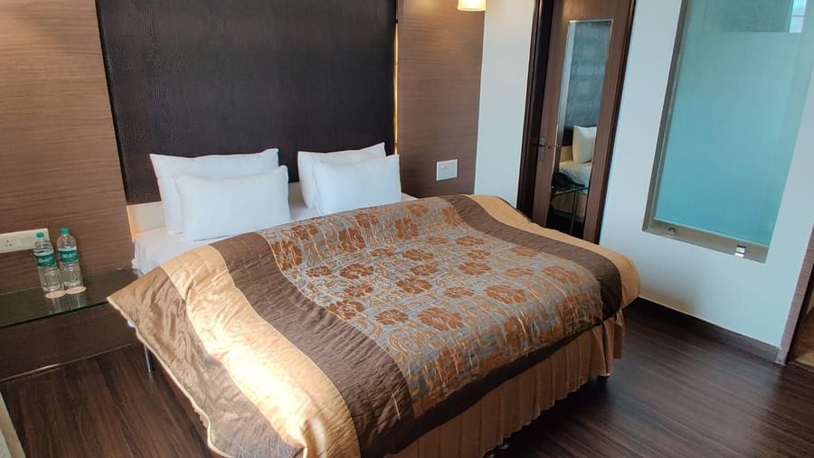 A bedroom with a neatly made bed, dark curtains, and a wooden floor, creating a comfortable space - VITS Gurugram
