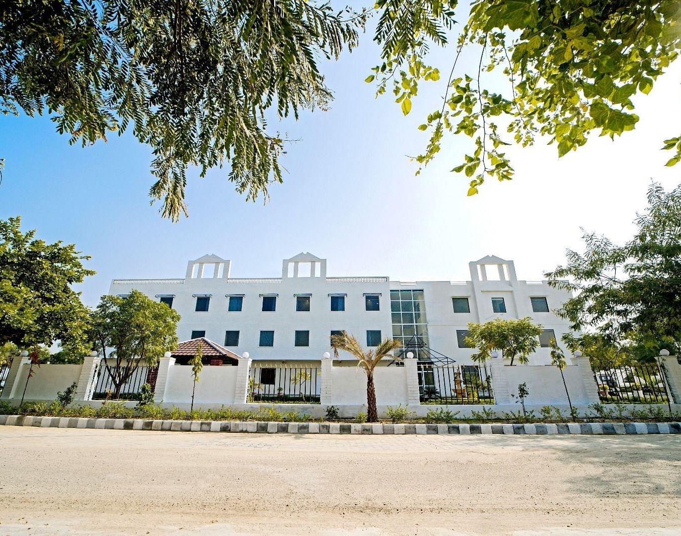 Front view of Grassfield Riveria Resort, Jaipur, surrounded by trees and clear skies, showcasing the modern building facade.