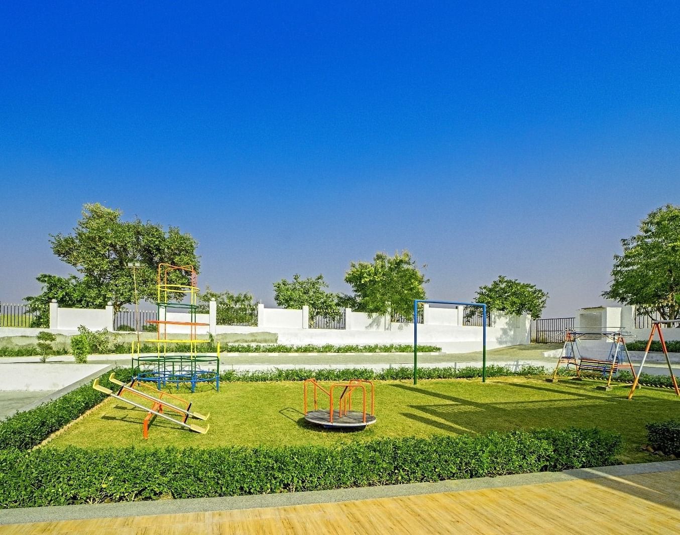 Children’s playground at Grassfield Riveria Resort, Jaipur, featuring swings, a roundabout, and lush greenery under a clear blue sky.