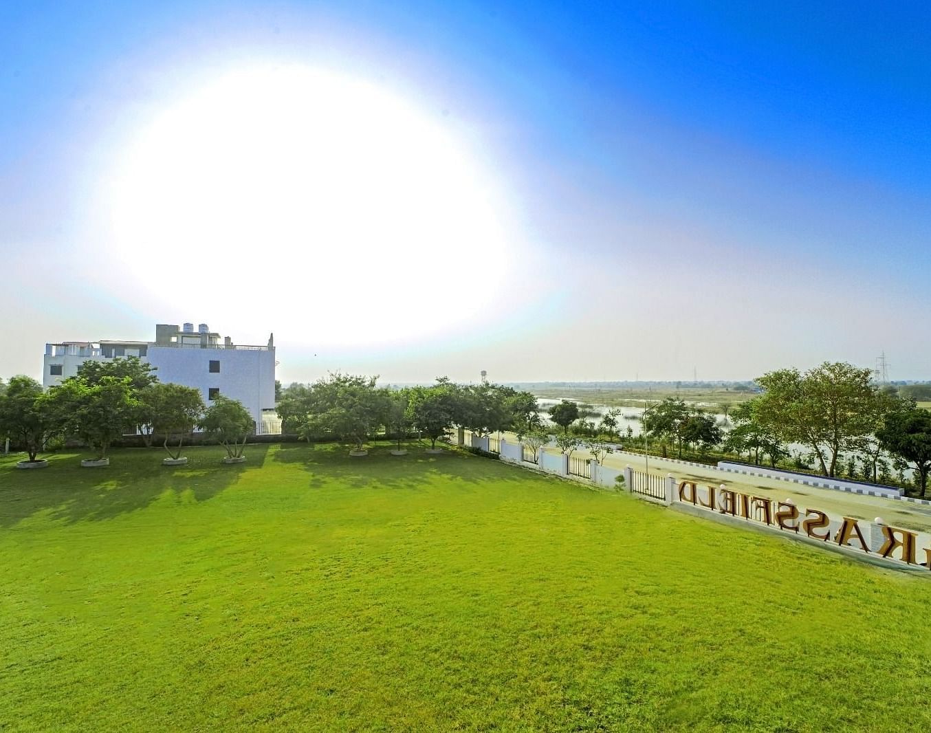 Expansive lawn and buildings at Grassfield Riveria Resort, Jaipur, under a bright sky with distant landscape views.