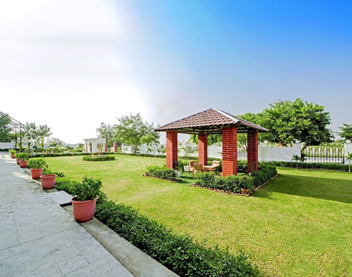Tranquil garden area at Grassfield Riveria Resort, Jaipur, featuring a small gazebo, manicured lawns, and potted plants along the pathway.