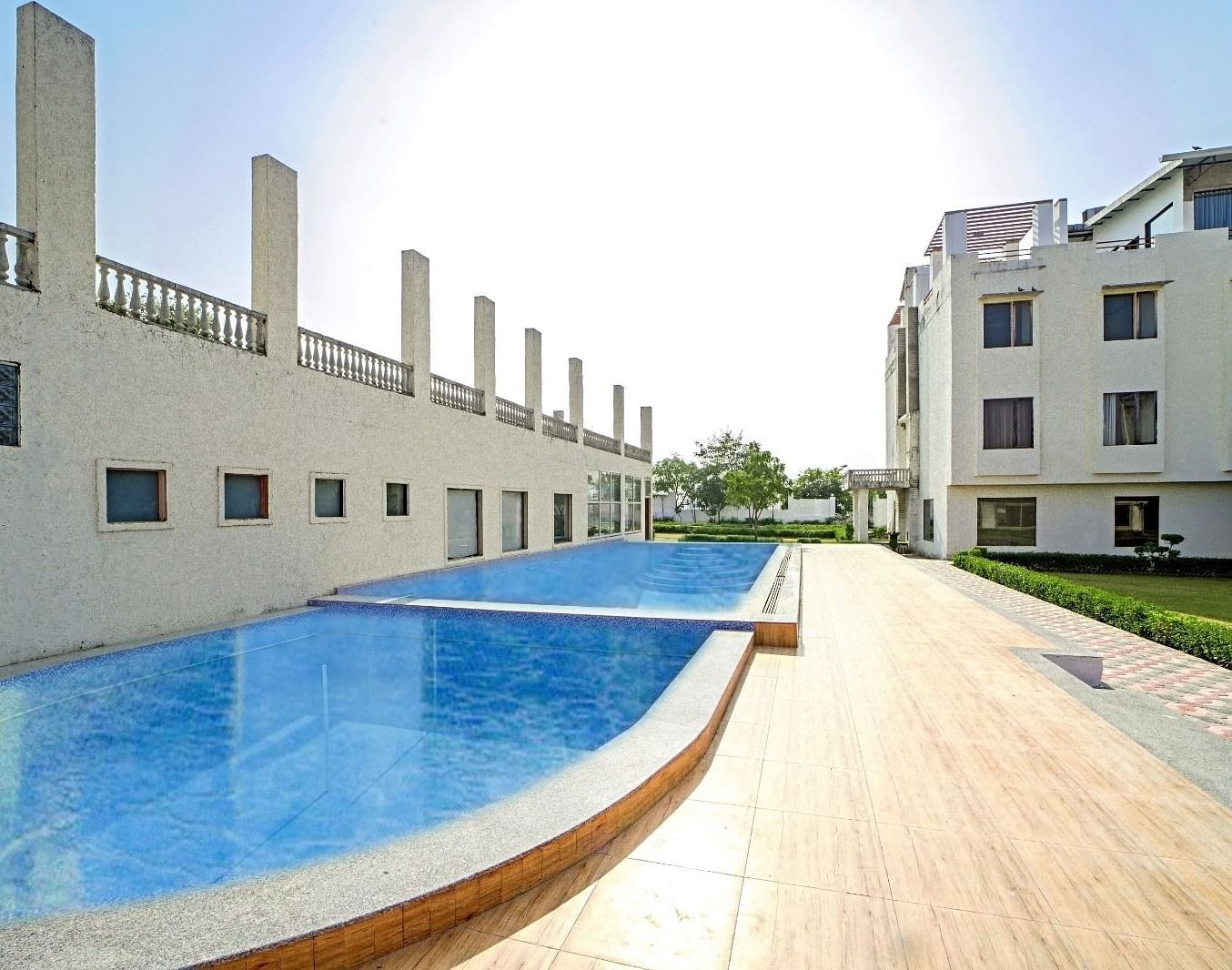 Outdoor swimming pool at Grassfield Riveria Resort, Jaipur, featuring clear water and a wooden deck under bright sunlight.