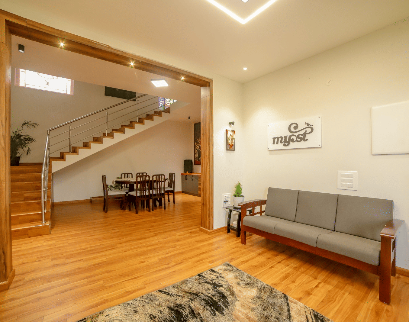 An upholstered multi-seater sofa seen in the living area of MYST Resorts, Doddabetta, Ooty, seen on wooden flooring, and the dining table seen in another section of the villa.