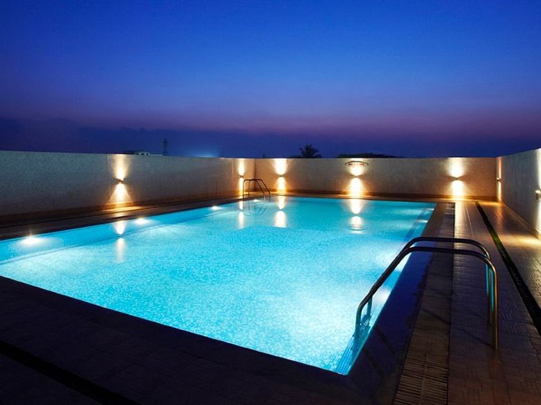 An image of an outdoor swimming pool installed with dim lights on the sides of it - Hotel Pai Vista, Mysore