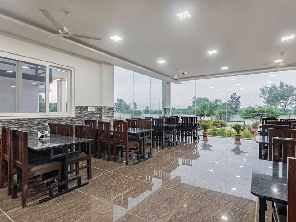 Well-lit restaurant with large windows offering scenic views and comfortable wooden seating at Siri Ambari Resorts and Spa.