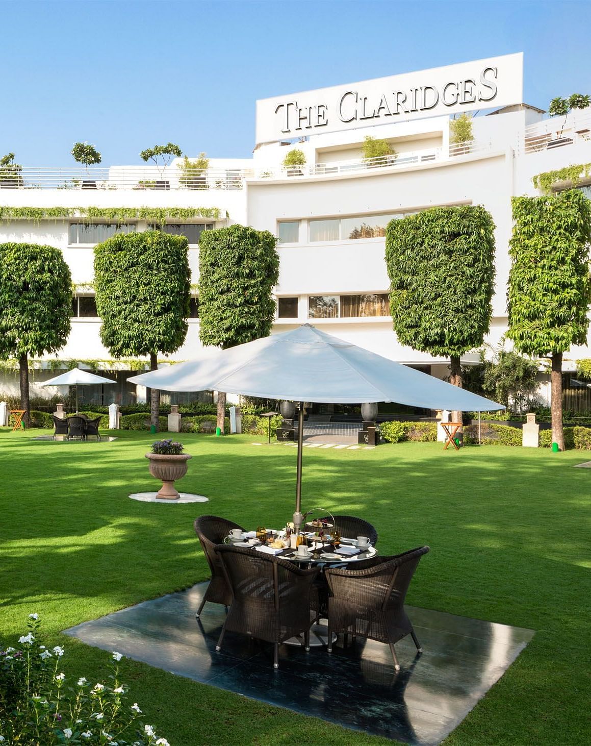 a beautiful landscape image of the claridges garden with glass top coffee tables scattered everywhere - The Claridges New Delhi