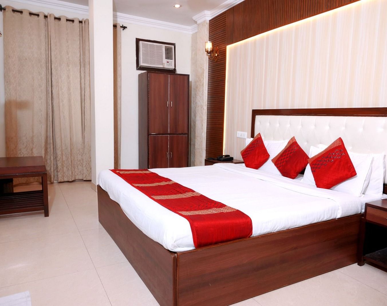 A stylish hotel room with a king-size bed, red and white linens, wooden furnishings, and elegant lighting - Hotel Diamond Inn, Chandigarh