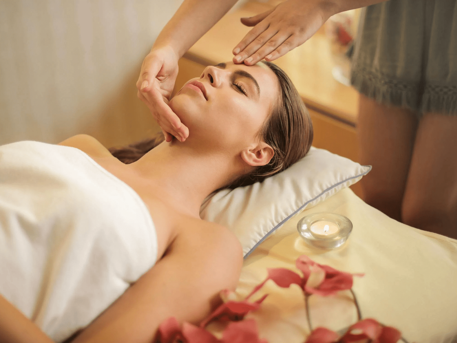 Woman wrapped in a towel lying on a bed and getting a massage.
